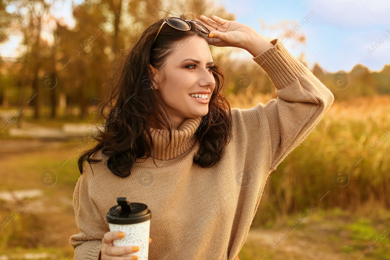 Photo of Beautiful young woman with cup of coffee wearing stylish autumn sweater outdoors