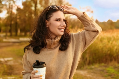 Photo of Beautiful young woman with cup of coffee wearing stylish autumn sweater outdoors