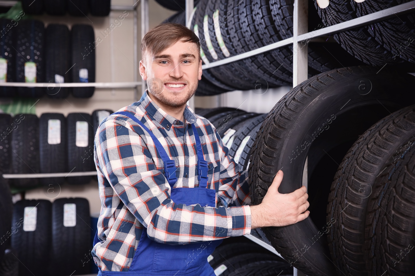 Photo of Young male mechanic with car tires in automobile service center