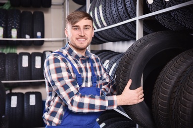 Young male mechanic with car tires in automobile service center