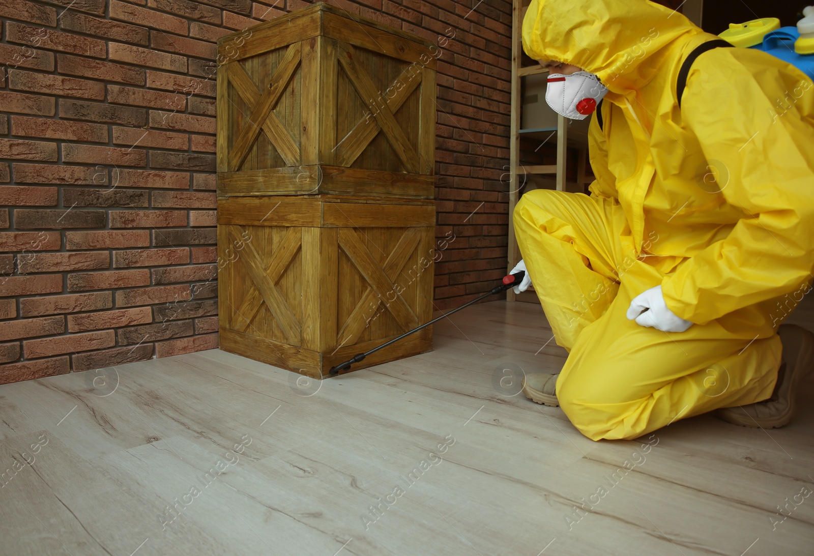 Photo of Pest control worker in protective suit spraying pesticide indoors