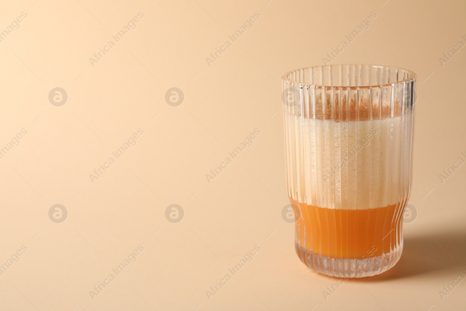 Photo of Glass of delicious eggnog on beige background. Space for text