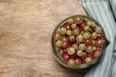 Jar of fresh ripe gooseberries on wooden table, top view. Space for text