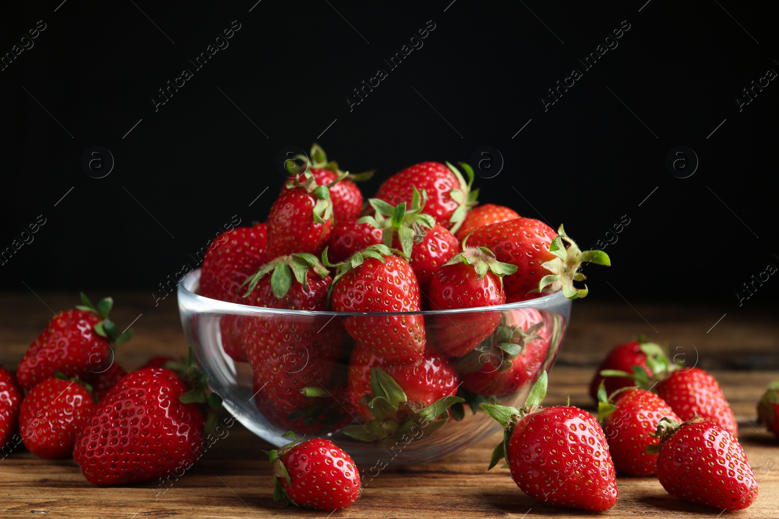 Photo of Delicious ripe strawberries in glass bowl on wooden table