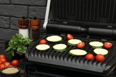 Photo of Electric grill with vegetables and spices on black table