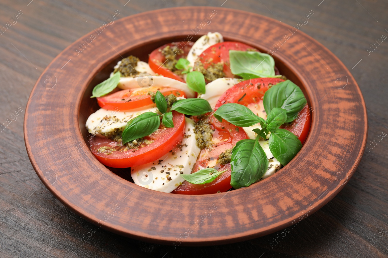 Photo of Plate of delicious Caprese salad with pesto sauce on wooden table, closeup