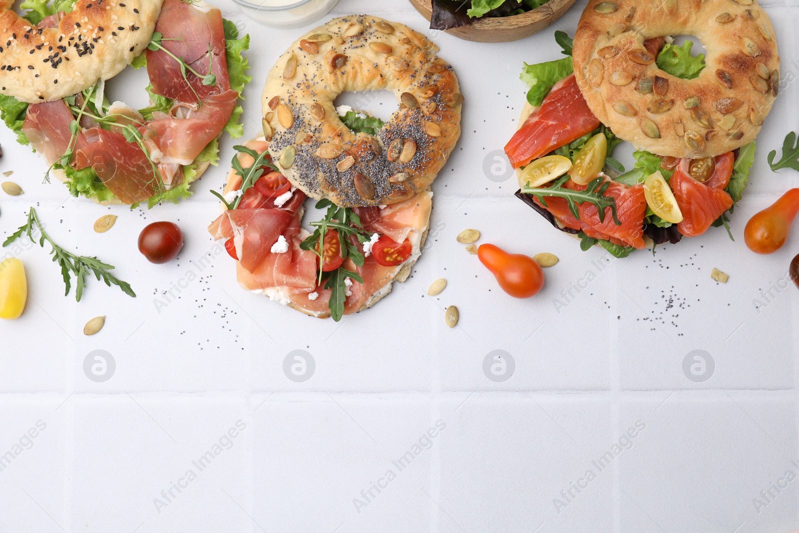 Photo of Tasty bagel sandwiches on white tiled table, flat lay. Space for text