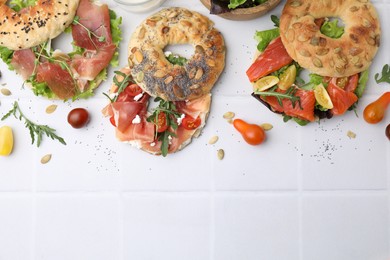 Photo of Tasty bagel sandwiches on white tiled table, flat lay. Space for text