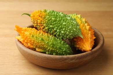 Photo of Bowl with fresh bitter melons on wooden table, closeup