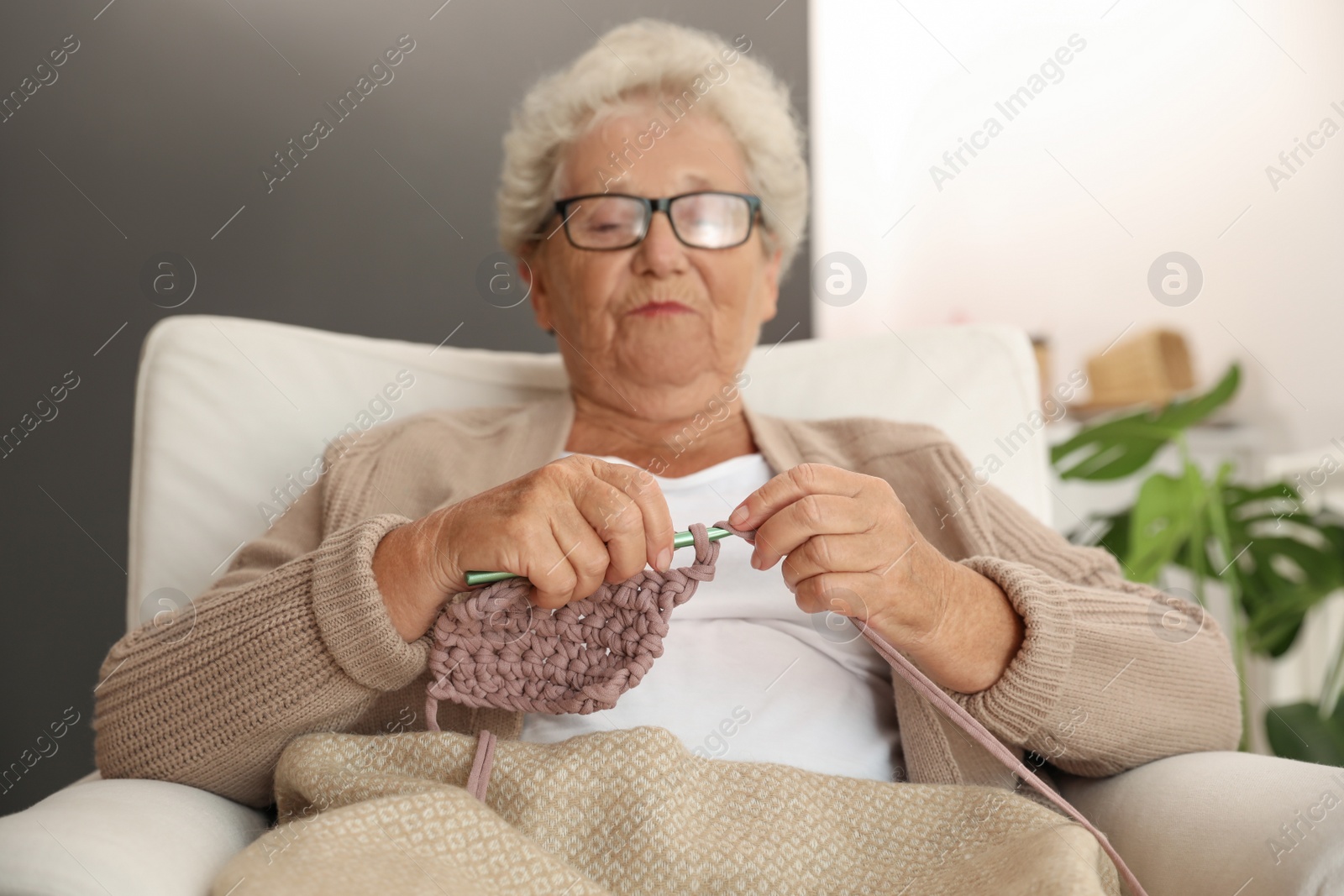 Photo of Elderly woman crocheting at home. Creative hobby