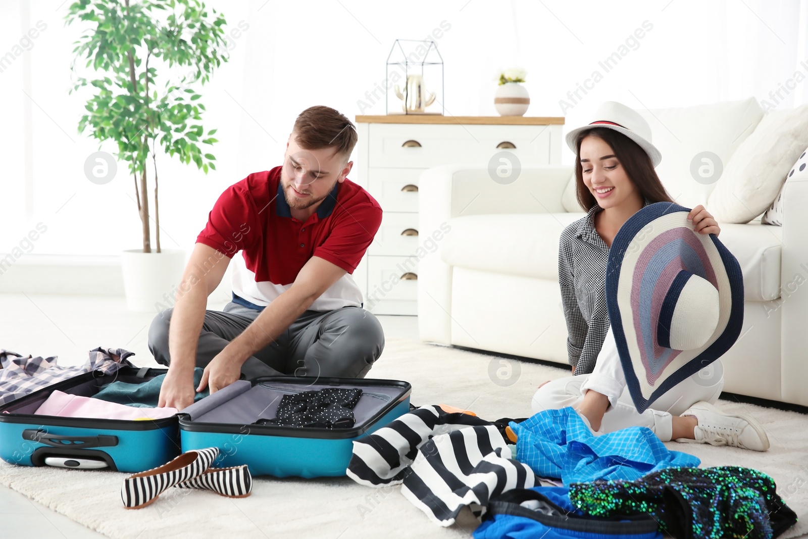 Photo of Young couple packing suitcase for summer journey at home