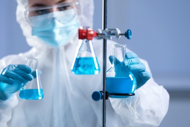 Scientist holding flasks with light blue liquid on grey background, focus on hands
