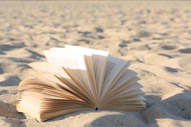 Photo of Open book on sandy beach, closeup view