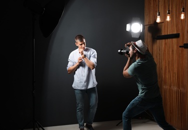 Professional photographer taking picture of young man on dark grey background in modern studio