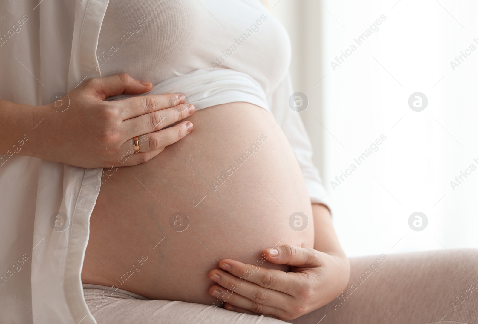 Photo of Pregnant woman sitting in light room at home, closeup