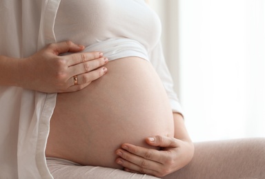 Pregnant woman sitting in light room at home, closeup