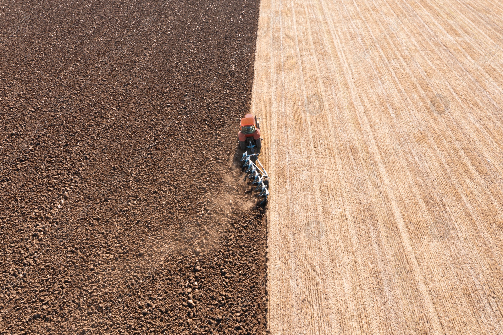 Image of Tractor pulling plow in agricultural field on sunny day, aerial view