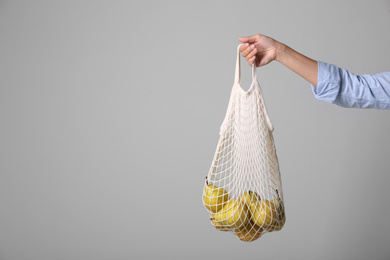 Photo of Woman holding net bag with fresh ripe pears on grey background, closeup. Space for text