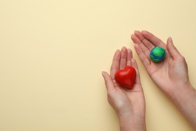 Photo of Woman holding model of planet and red heart on beige background, top view with space for text. Earth Day