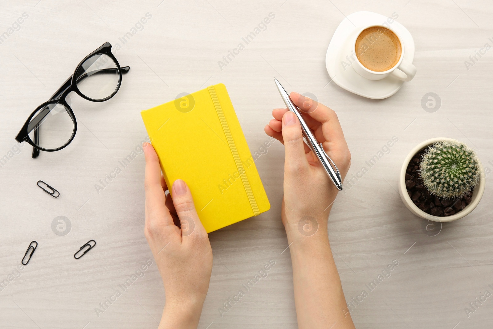 Photo of Woman with notebook and pen at light wooden table, top view