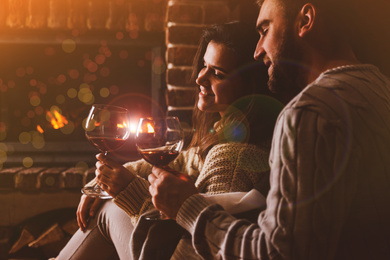 Lovely couple with glasses of wine near fireplace at home. Winter vacation