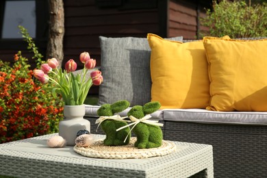 Photo of Terrace with Easter decorations. Bouquet of tulips in vase, bunny figures and decorated eggs on table outdoors