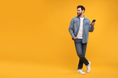 Photo of Smiling man with smartphone on orange background. Space for text