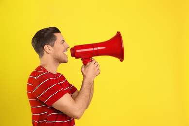 Handsome man with megaphone on yellow background. Space for text