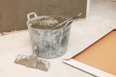 Photo of Bucket of adhesive mix and spatula on floor indoors Tiles installation process