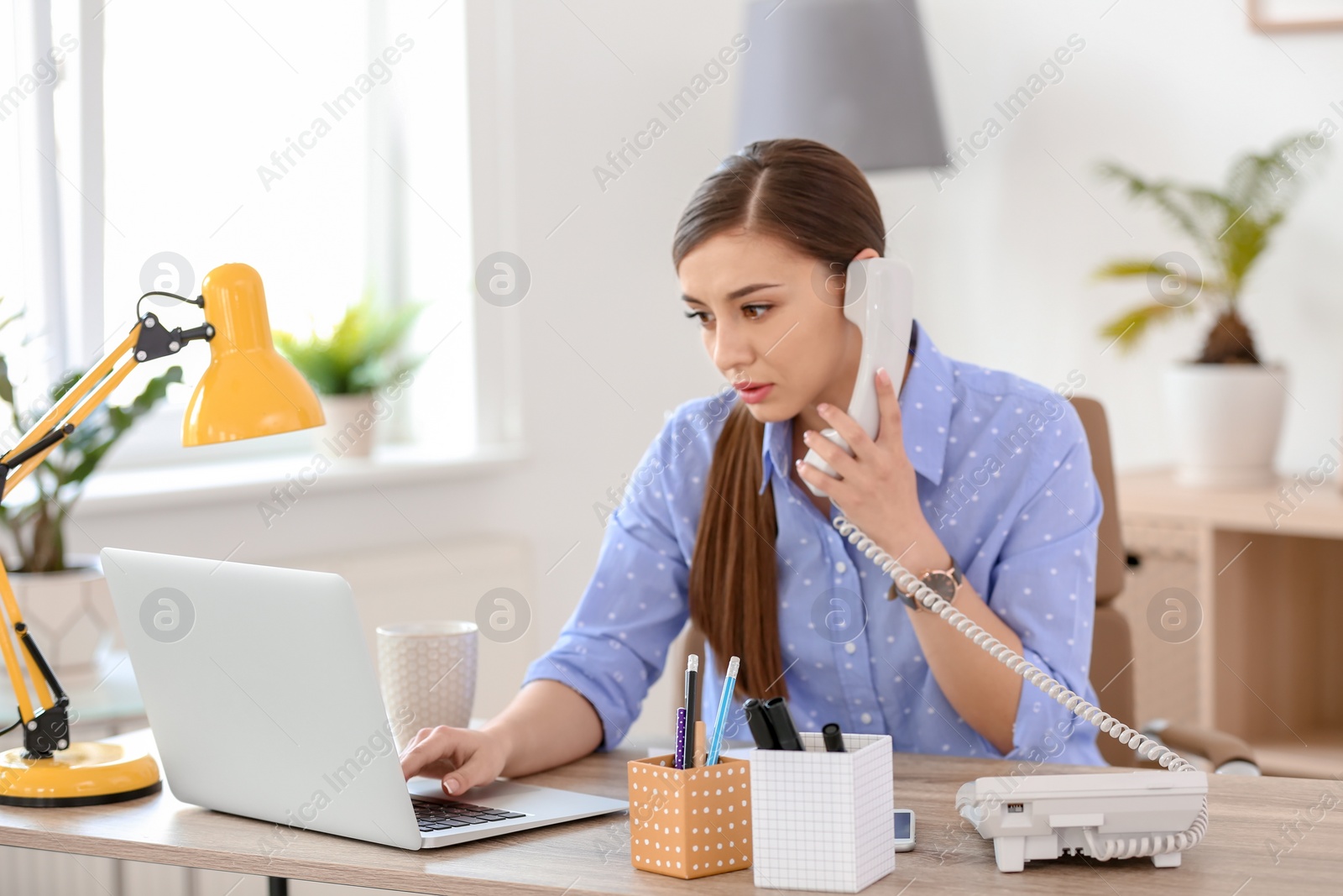 Photo of Young woman talking on phone at workplace