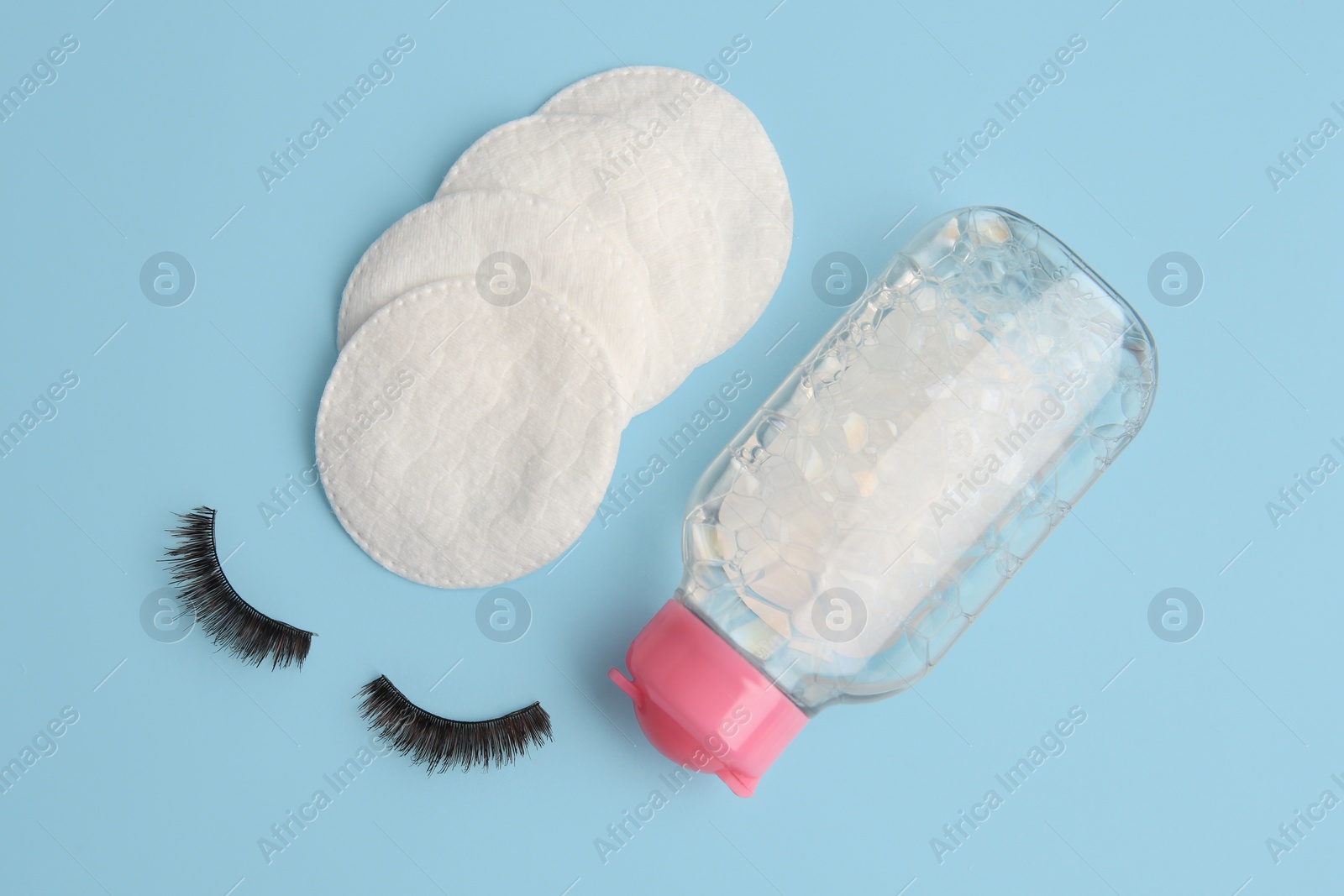 Photo of Bottle of makeup remover, cotton pads and false eyelashes on light blue background, flat lay