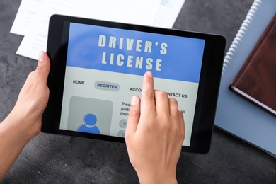 Person using tablet to fill driver's license application form at grey table, closeup