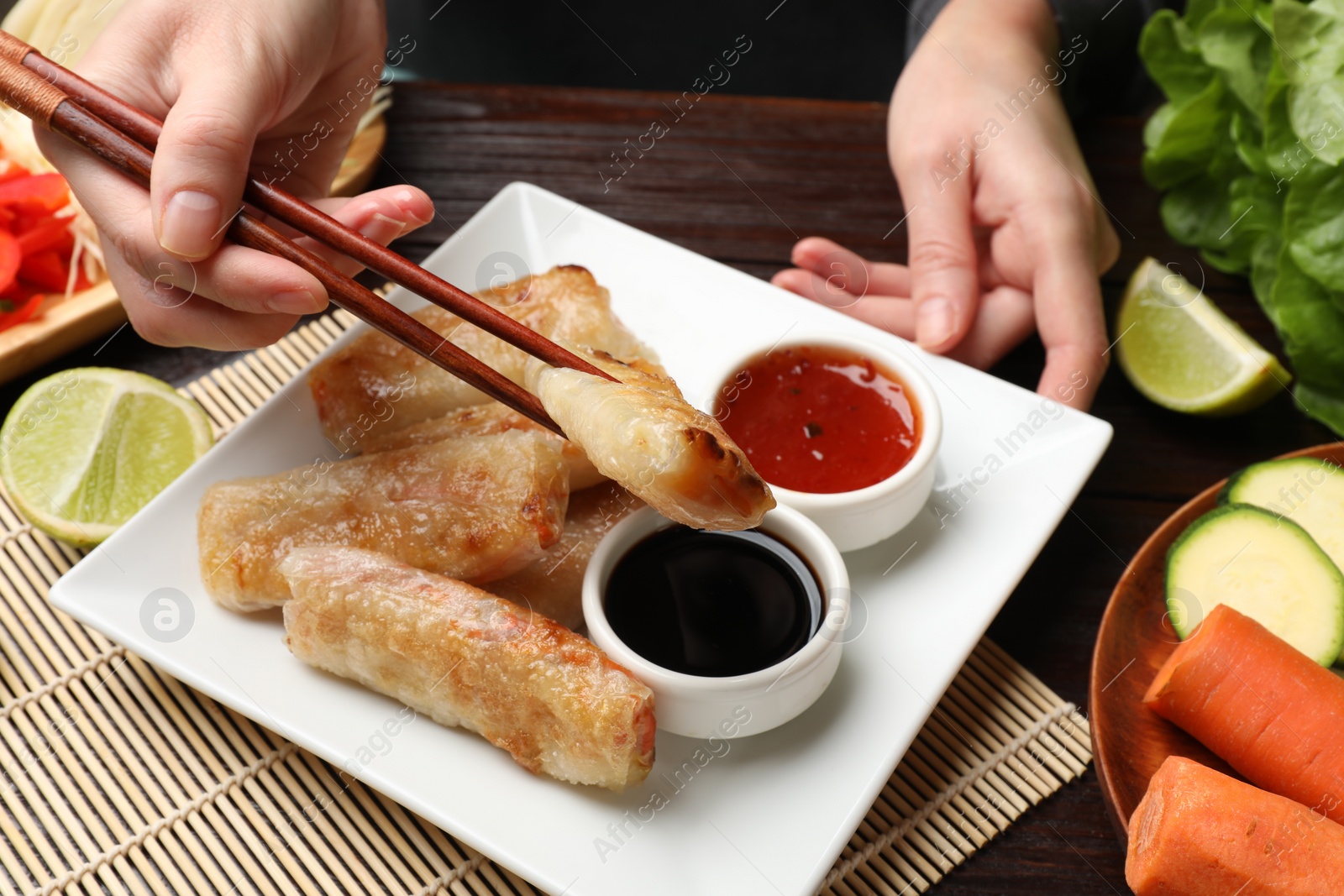 Photo of Woman eating tasty fried spring rolls at table, closeup