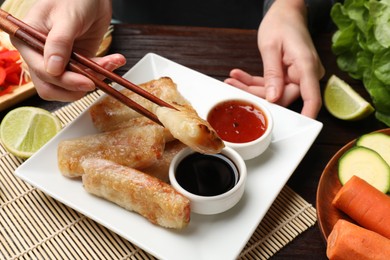 Woman eating tasty fried spring rolls at table, closeup