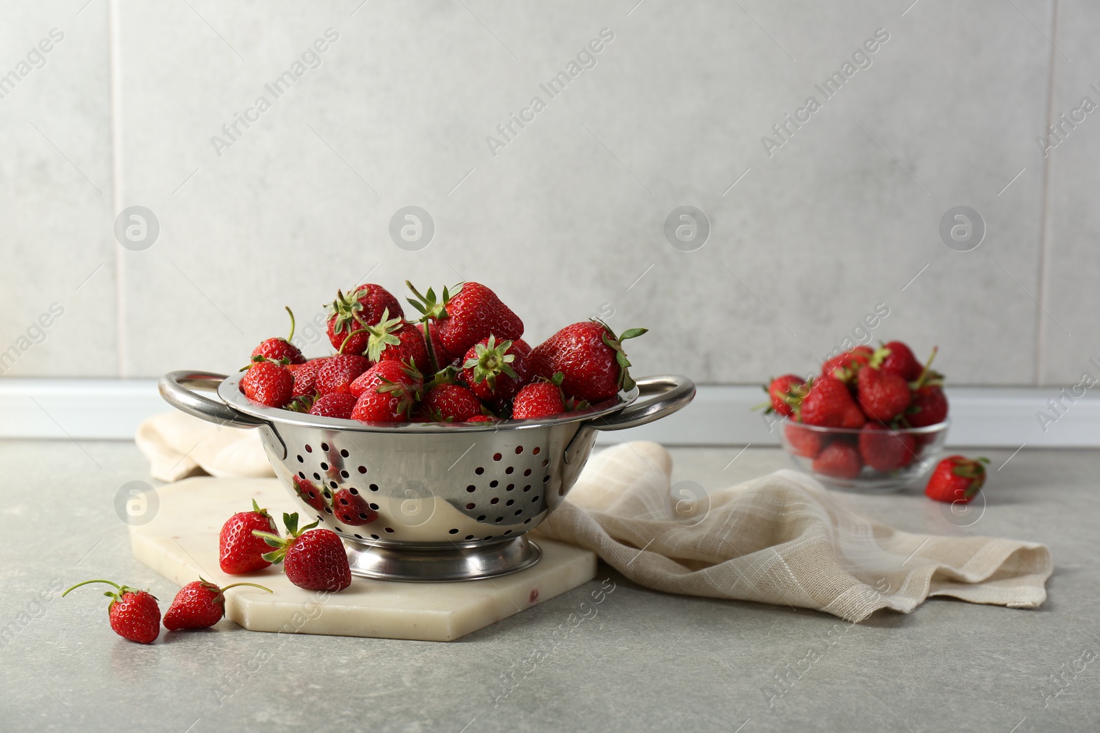 Photo of Metal colander with fresh strawberries on grey countertop