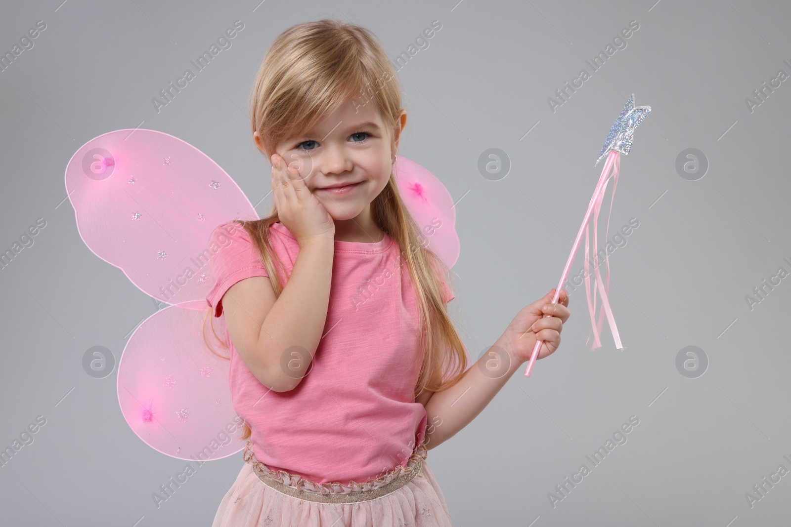 Photo of Cute little girl in fairy costume with pink wings and magic wand on light grey background