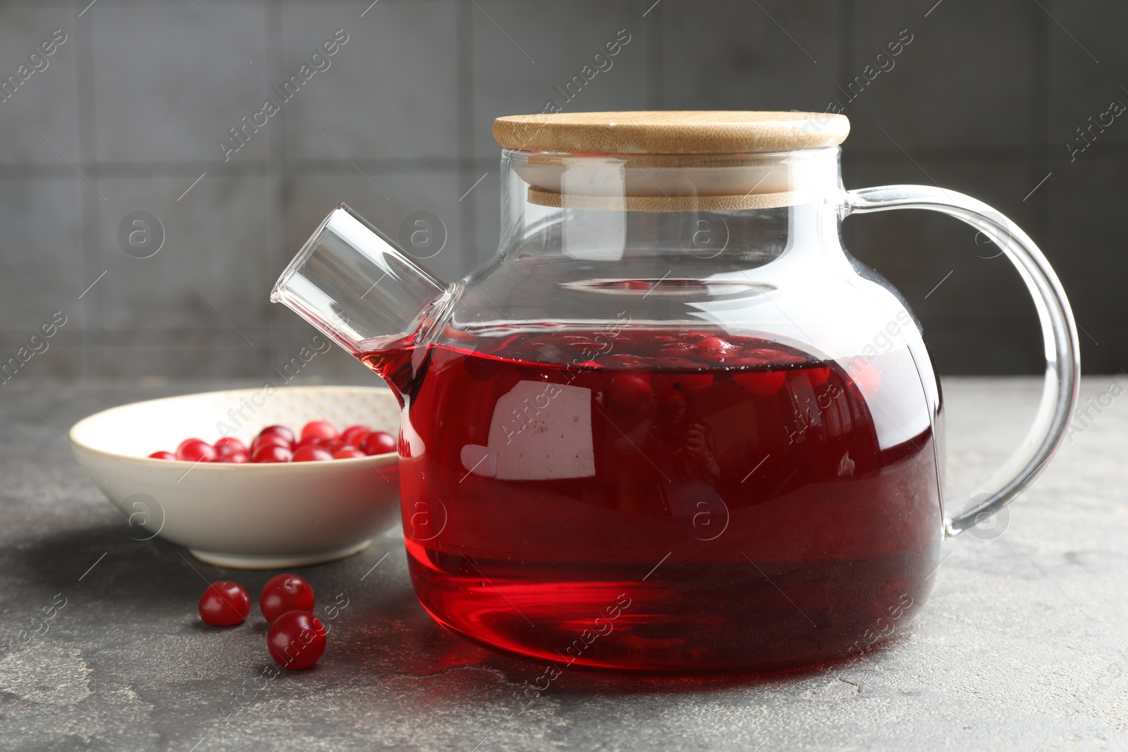 Photo of Tasty hot cranberry tea in teapot and fresh berries on light grey textured table