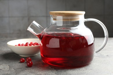 Tasty hot cranberry tea in teapot and fresh berries on light grey textured table