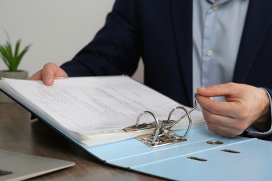 Photo of Businessman putting document into file folder at wooden table in office, closeup