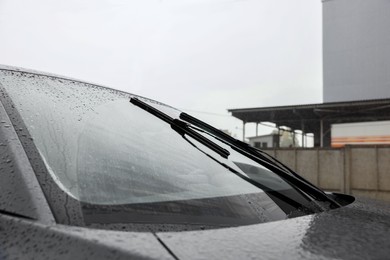 Car wipers cleaning water drops from windshield glass outdoors, closeup