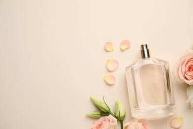 Photo of Flat lay composition of bottle with perfume and fresh flowers on beige background, space for text