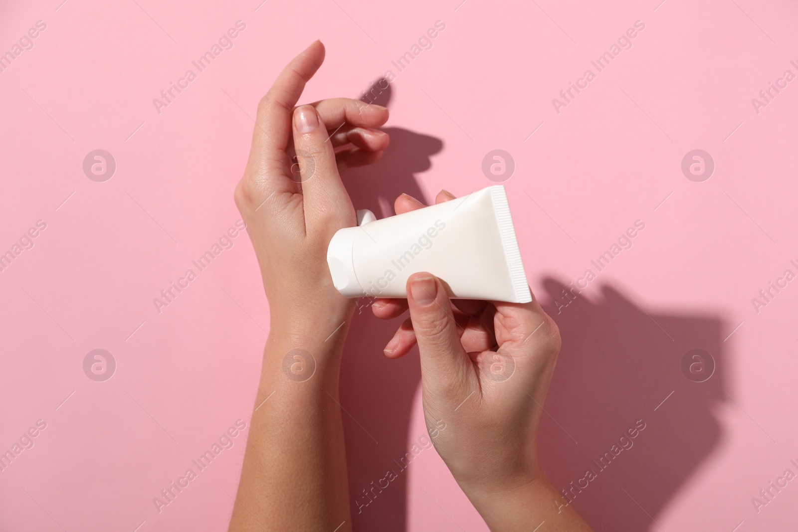 Photo of Woman applying cosmetic cream from tube onto her hand on pink background, top view