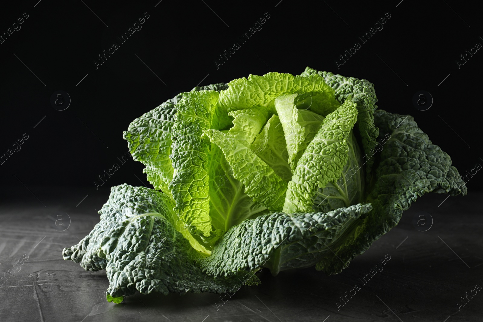 Photo of Fresh green savoy cabbage on grey table against black background