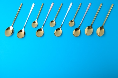 New gold spoons on blue background, flat lay with space for text