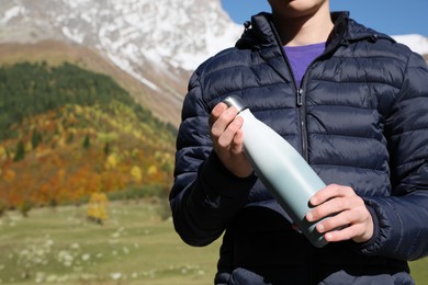 Photo of Boy holding thermo bottle with drink in mountains on sunny day, closeup. Space for text