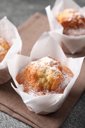 Photo of Delicious muffins with powdered sugar on grey table, closeup