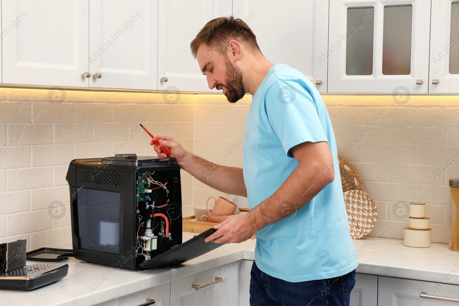 Photo of Man with screwdriver fixing coffee machine at table in kitchen