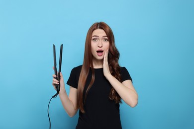 Emotional woman with hair iron on light blue background