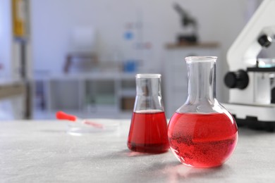 Photo of Laboratory analysis. Flasks with red liquid, petri dish and microscope on light grey table