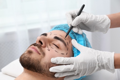 Doctor drawing marks on man's face for cosmetic surgery operation in clinic